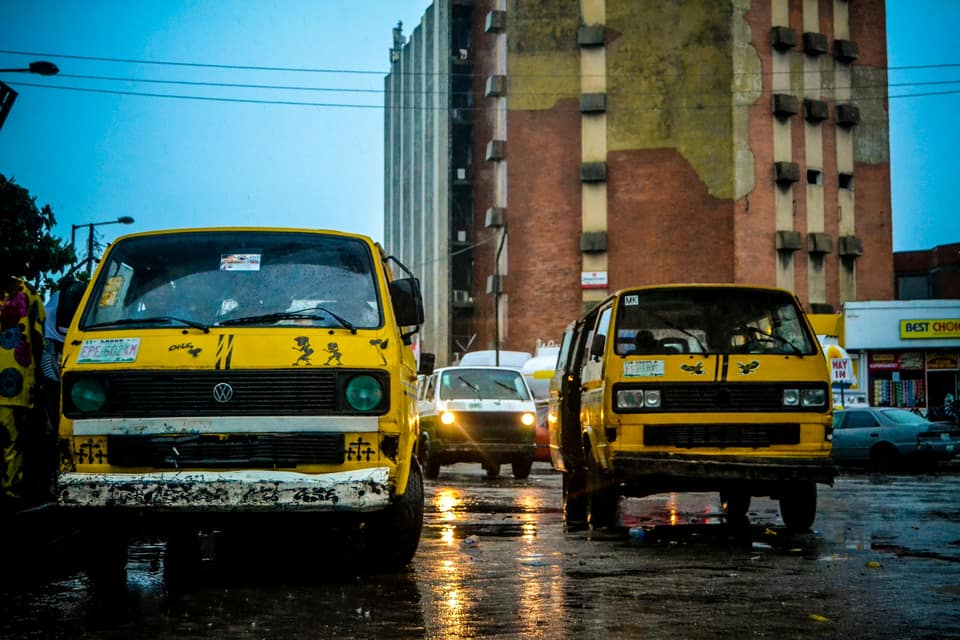 Two yellow buses parked on a wet Lagos street